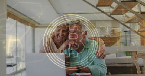 Senior couple researching Bitcoin on laptop at home with holographic crypto coin overlay
