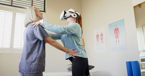 Physical therapist assisting woman with prosthetic leg using vr