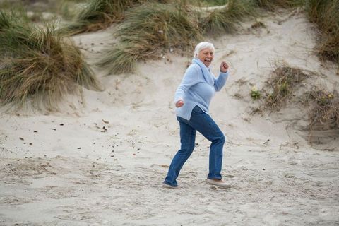 Senior woman enjoying stroll on serene beach, surrounded by dune grass
