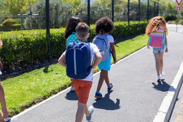 Rear view of group of kids with backpacks walking on footpath. school education social distancing quarantine lockdown during coronavirus pandemic