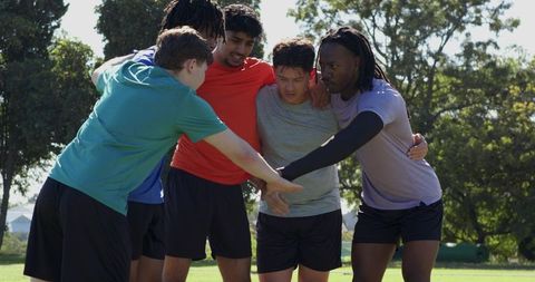 Multiracial male teammates forming energetic huddle on sunlit field boosting team unity