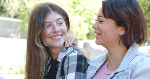 Diverse friends sharing warm conversation on sunlit park bench in garden, denim jacket, plaid shirt