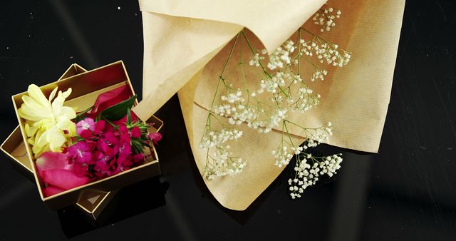 A selection of vibrant flowers is presented in an open gift box, complemented by delicate baby's breath on a draped beige fabric, with copy space. The arrangement suggests a special occasion or a thoughtful gift, capturing a sense of elegance and celebration.