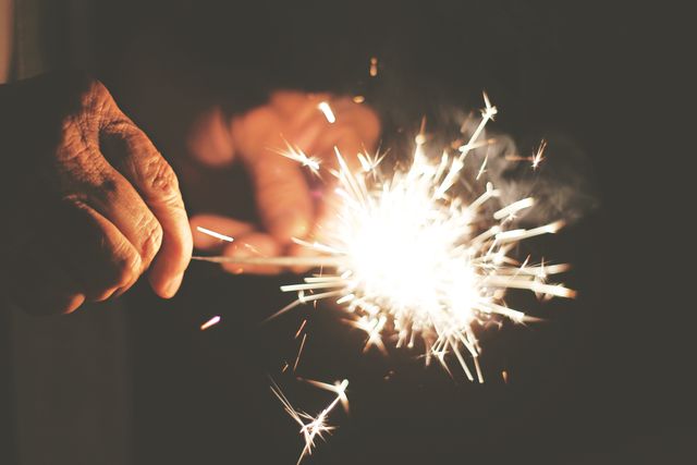 Hand holding a burning sparkler, creating a bright, festive atmosphere against a dark background. Perfect for themes of celebration, joy, holidays, festivals, and new year. Suitable for advertisements, greeting cards, event promotions, and festive social media content.