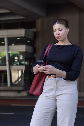 African american commuter checking smartphone at public transit entrance with red tote bag