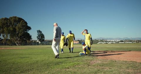 Baseball team regrouping on infield with seated player, coach walking, yellow uniforms