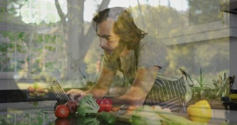 Leaning man wearing striped apron cooking and using tablet while prepping fresh vegetables