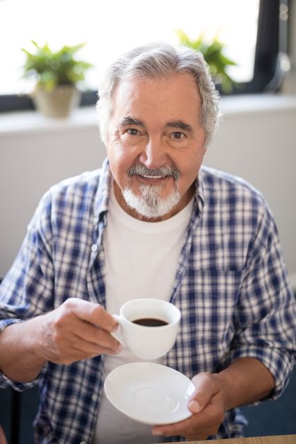 Portrait of smiling senior man holding coffee cup while sitting at nursing home