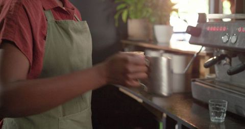 Barista woman pouring steamed milk from stainless pitcher by espresso machine in cafe