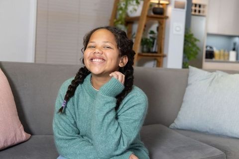 Smiling girl sitting on gray couch wearing teal sweater in cozy open-plan living room