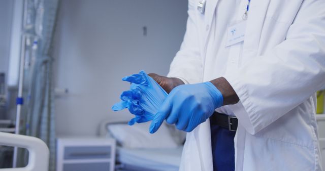 Midsection of african american male doctor wearing latex gloves in hospital patient room. medicine, health and healthcare services.
