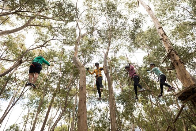 Group of friends participating in a zip line adventure in a forest park on a sunny day. Ideal for promoting outdoor activities, team-building events, adventure tourism, and recreational parks.