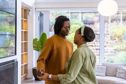 African american couple holding hands dancing in sunlit modern living room