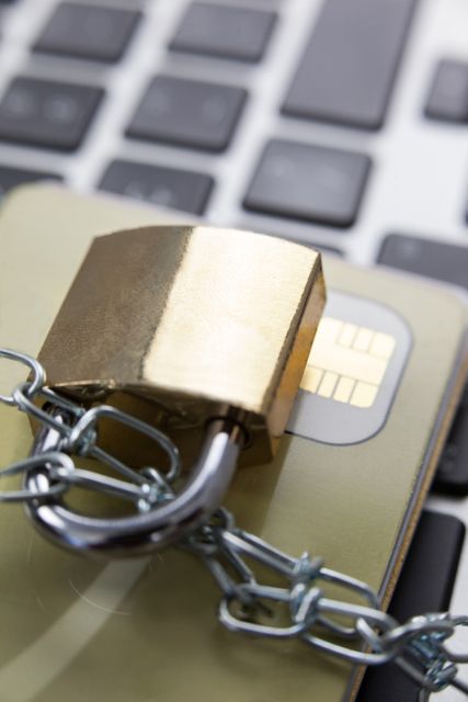 Close-up of a smart card secured with a chain and padlock on a laptop keyboard. This image can be used to represent cybersecurity, data protection, encryption, and secure online transactions. Ideal for articles, blogs, and presentations on digital security, financial safety, and technology.
