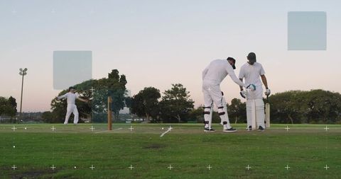 Dusk cricket match with fast bowler delivering ball and two batsmen preparing at crease