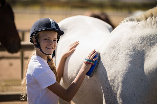 Smiling girl grooming the horse in the ranch on a sunny day