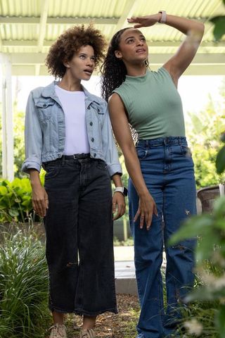 African american friends standing under pergola shading eyes and looking into garden