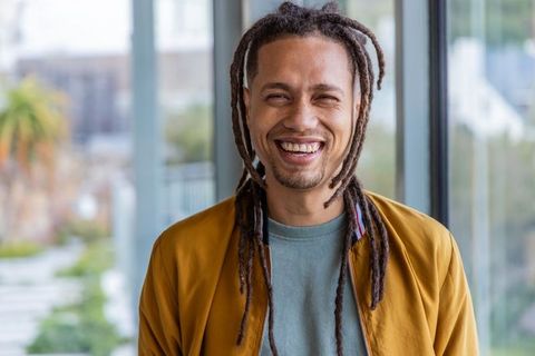 Smiling man with dreadlocks and goatee wearing mustard jacket in modern coworking space