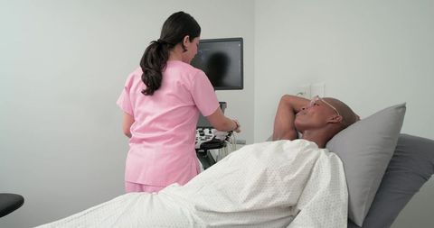 Sonography technician adjusting ultrasound monitor while patient lying on examination bed