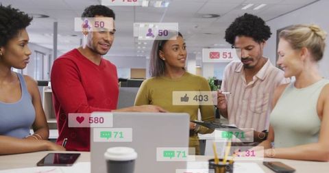 Diverse team collaborating around laptop with social media metrics overlays in open office