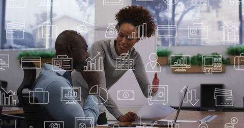 African american colleagues collaborating at office desk pointing to documents by laptop