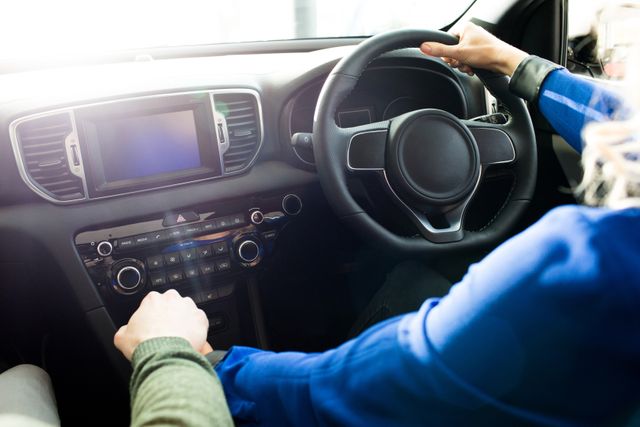 Couple holding hands while test driving a new car in a showroom. The image showcases the car's modern dashboard and steering wheel, highlighting the vehicle's interior features. Ideal for use in automotive advertisements, car dealership promotions, and articles about car buying experiences.