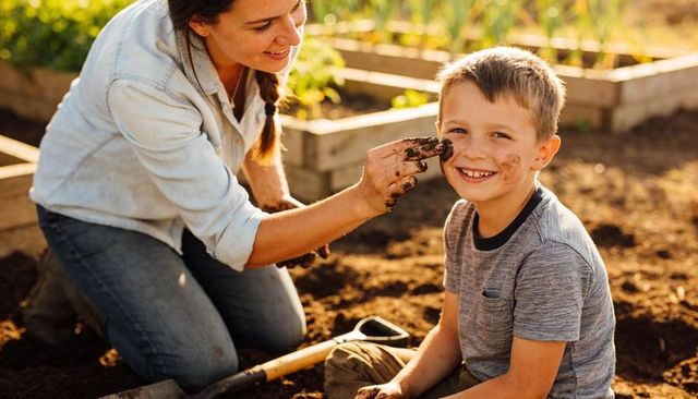 Mother and son gardening together smearing soil and smiling in sunlit backyard