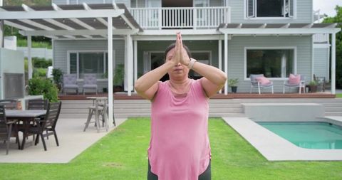 Mature woman practicing mindful yoga by pool in modern backyard patio with pergola