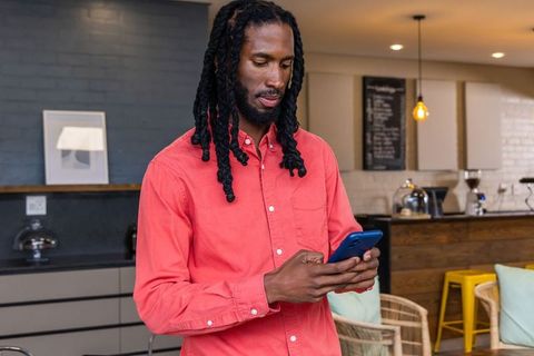 African american man checking smartphone in modern coffeehouse wearing coral shirt