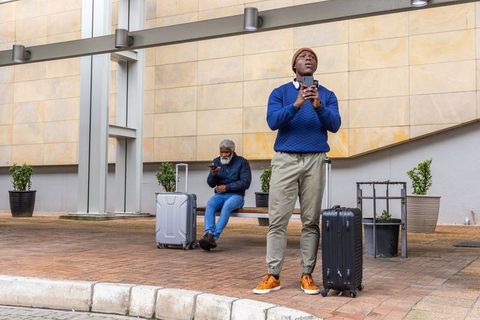 Urban travelers waiting with suitcases and smartphones at modern transit plaza
