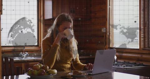 Cozy remote work in rustic cabin woman sipping coffee using laptop at wooden kitchen counter