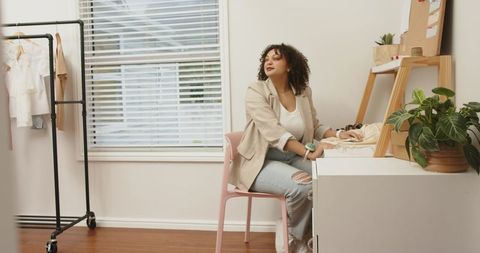 Woman in twenties designing boutique clothing in bright home studio workspace