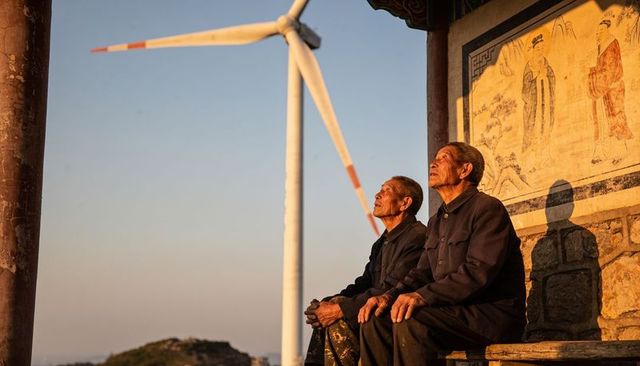 Elderly men sitting on pavilion bench at sunset with wind turbine and mural backdrop