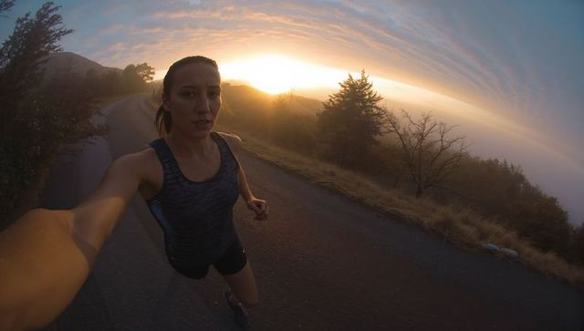 Female runner taking selfie on misty hillside road at golden sunrise glow