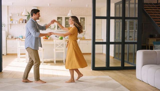 Barefoot couple dancing in sunlit open-plan kitchen living space, romantic home lifestyle