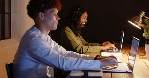 Diverse Colleagues Collaborating in Office at Night Using Laptops