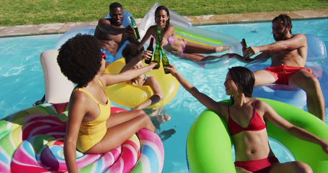Diverse group of friends having fun playing on inflatables making a toast in swimming pool. hanging out and relaxing outdoors in summer.