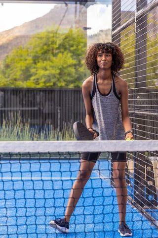 Athletic woman playing padel on blue outdoor court, readying to serve with paddle and ball