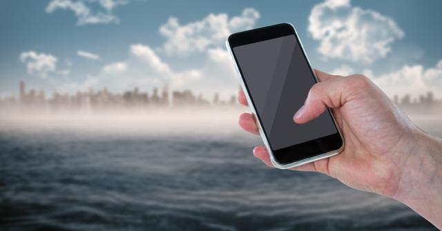 A person holding a smartphone with an out-of-focus urban skyline and water in the background. Suitable for themes related to technology, urban living, communication, and connecting in modern environments. Can be used in advertisements, articles on mobile technology or apps, and promotions targeting urban professionals.