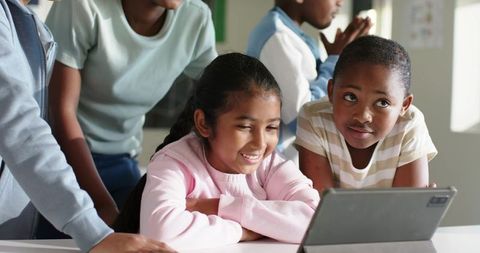 Elementary students collaborating around tablet, smiling and learning in sunlit classroom