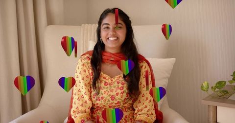 Smiling indian woman wearing yellow kurta and red dupatta sitting with rainbow hearts
