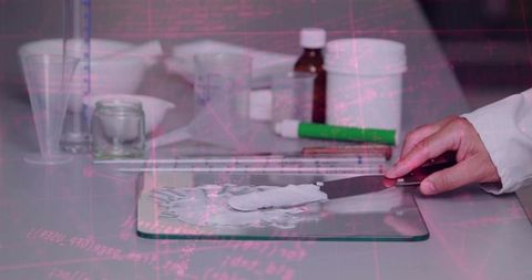Pharmacist compounding topical ointment on glass slab using spatula in laboratory