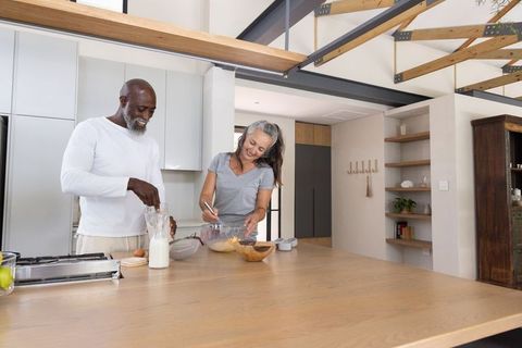 Mature diverse couple cooking together at bright modern open-plan kitchen island