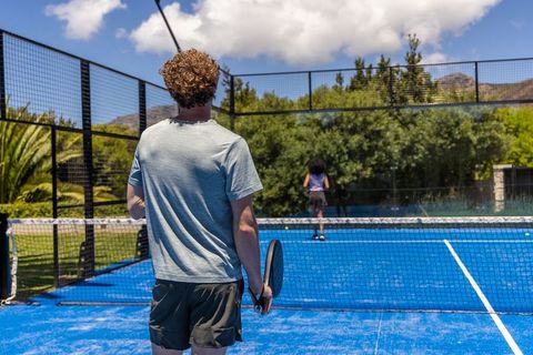 Couple playing paddle tennis on bright blue court with mountain backdrop and lush greenery