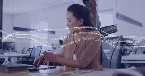Korean woman organizing device cables at desk in modern open office with data wave overlay