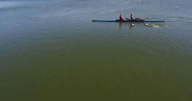 Two individuals rowing a canoe on a calm lake, creating ripples in the water. Ideal for illustrating themes of outdoor sports, teamwork, fitness, and peaceful natural settings. Suitable for advertisements, articles, or presentations related to water-based activities, adventure trips, or promoting healthy lifestyles.
