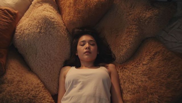 Asian woman resting on plush shag pillows in cozy bedroom, warm textured comfort and calm