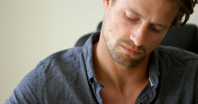 Young man seen intently writing notes while seated at a desk. Ideal for use in professional settings, education, workplace environments, and focus-driven projects.