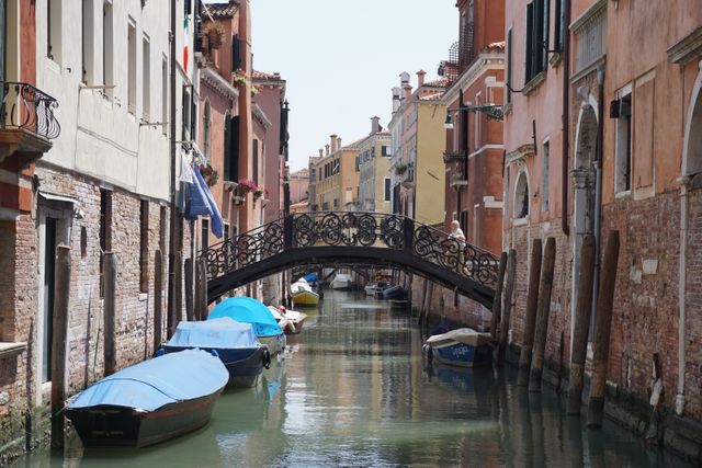 This serene view of a Venetian canal showcases the charm of the historic city with its classic architecture and a bridge crossing over the waterway. Ideal for marketing materials promoting travel and tourism in Europe, articles about Venice, or decorative prints capturing the unique beauty of Venice's waterways.