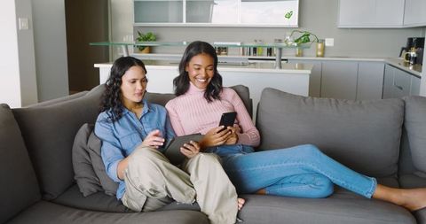 Diverse women enjoying modern technology on comfortable couch